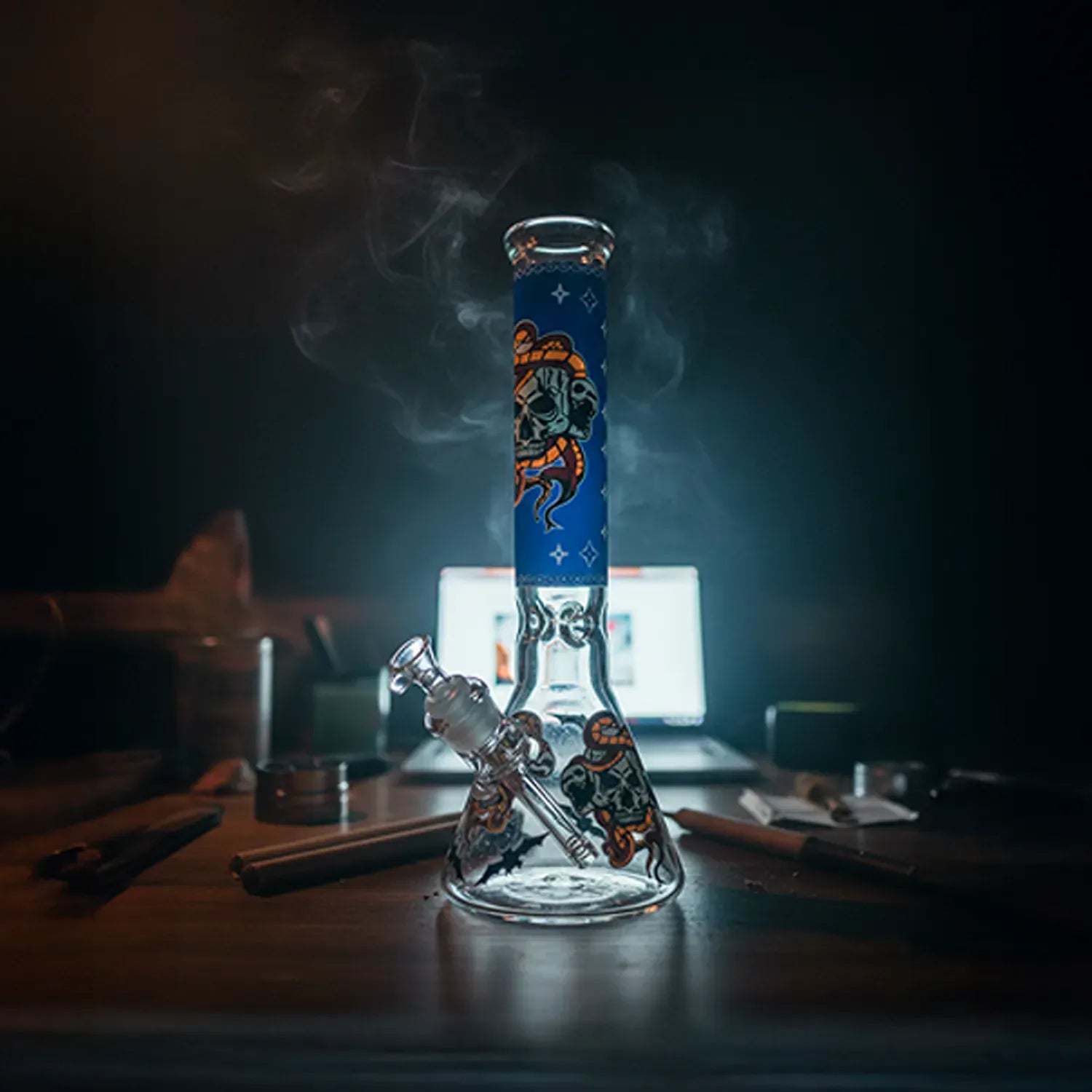 Center-framed, backlit shot of the Beaker Ice Bong with Glow in the Dark Snake and Skull Print standing on a tabletop with smoke drifting upward.