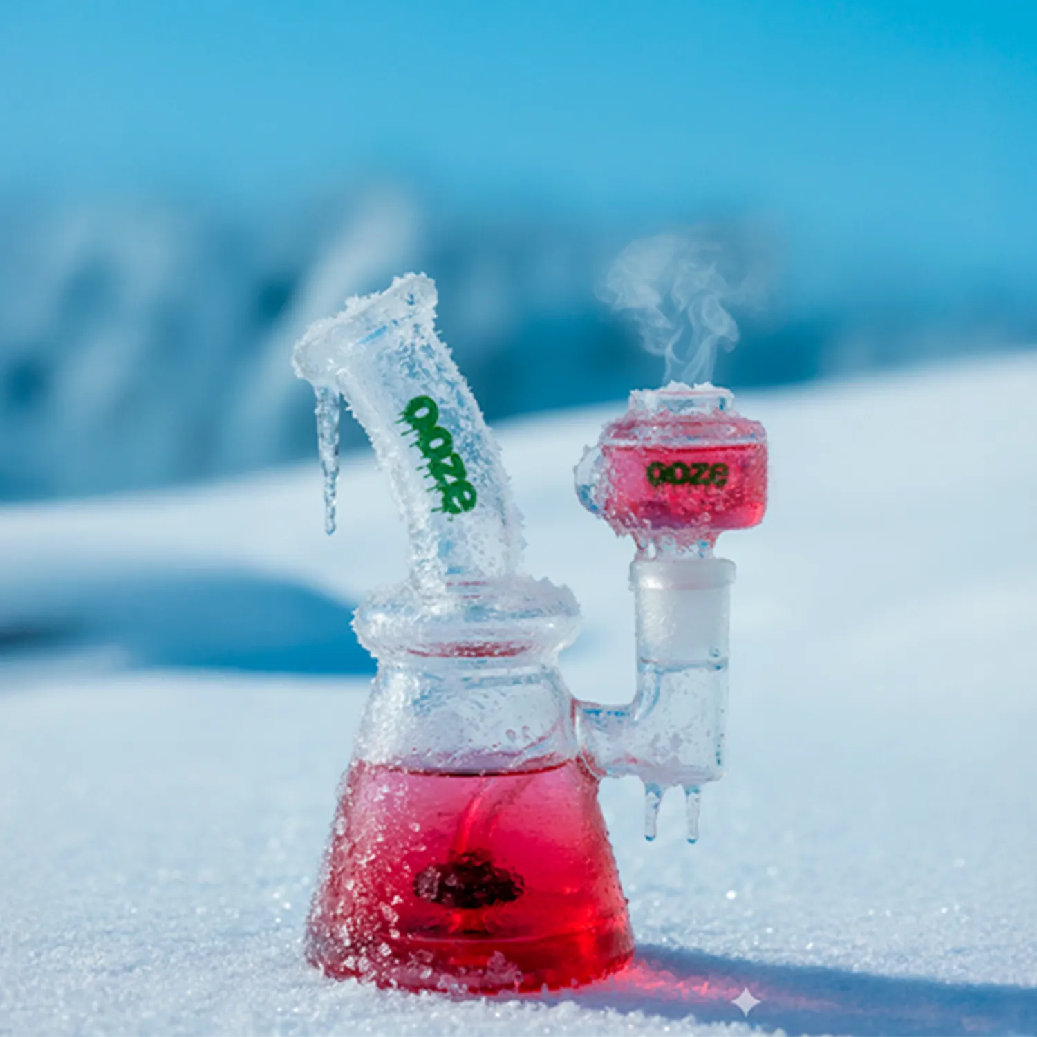 Close-up of the Ooze Glyco Bong Glycerin Chilled Glass Bong set in snow, showing a frosted scarlet beaker base and icy mouthpiece with steam rising.