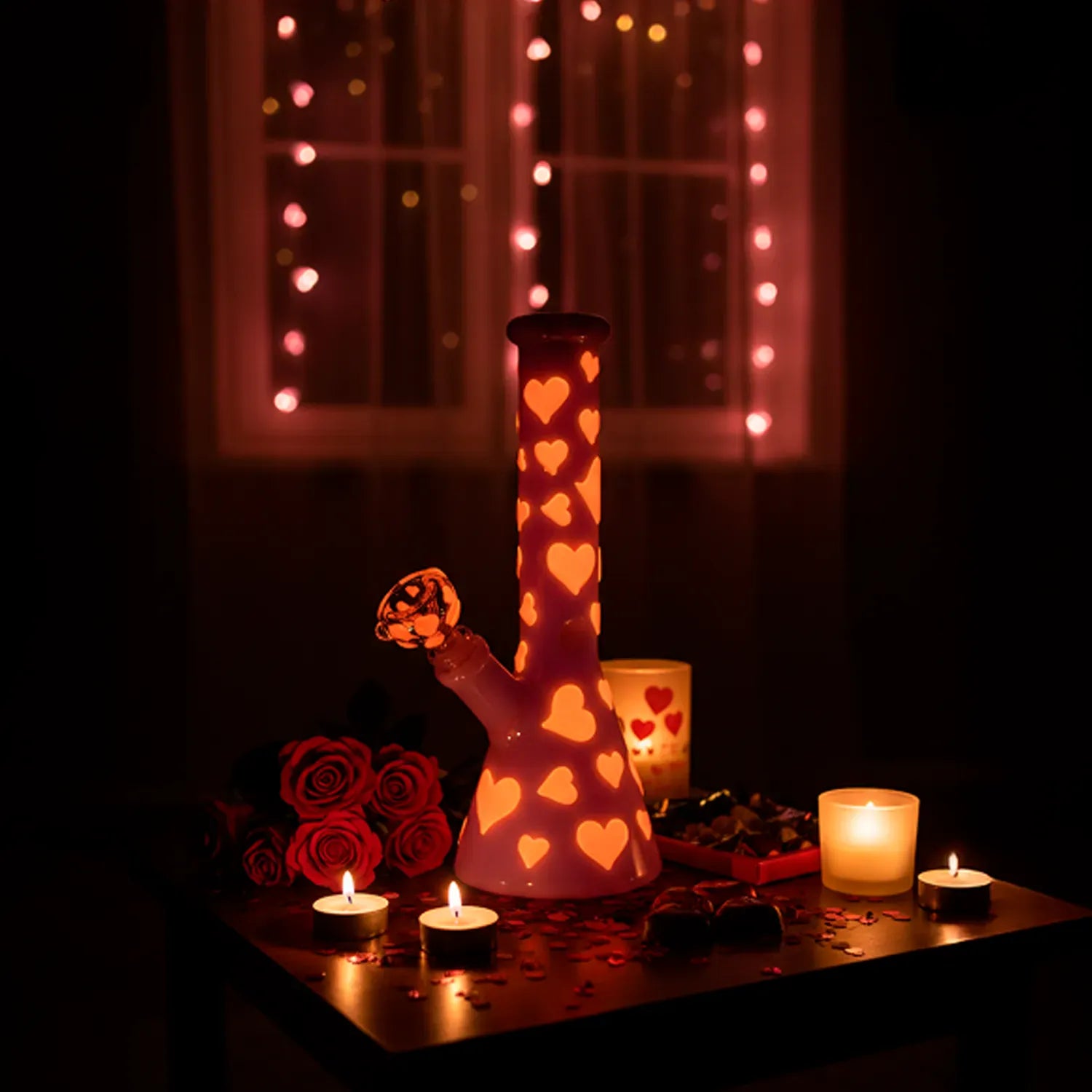 Centered frontal view of the 10" Valentines Day Heart Glow In The Dark Beaker Bong lit from within, surrounded by candles, roses, and string lights.