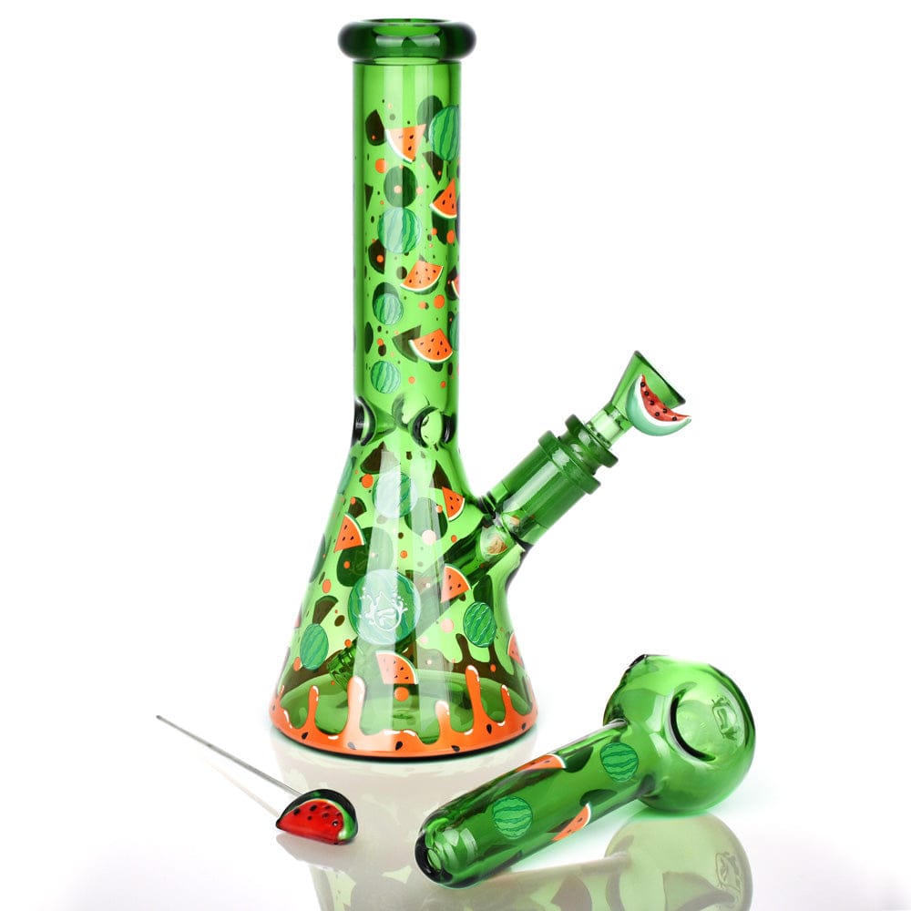 Studio-lit, front view of the Pulsar Fruit Series Watermelon Zkittles Herb Pipe Glow Duo - 10" / 14Mm F displaying a green beaker with watermelon slice motifs, matching spoon and nail on white.