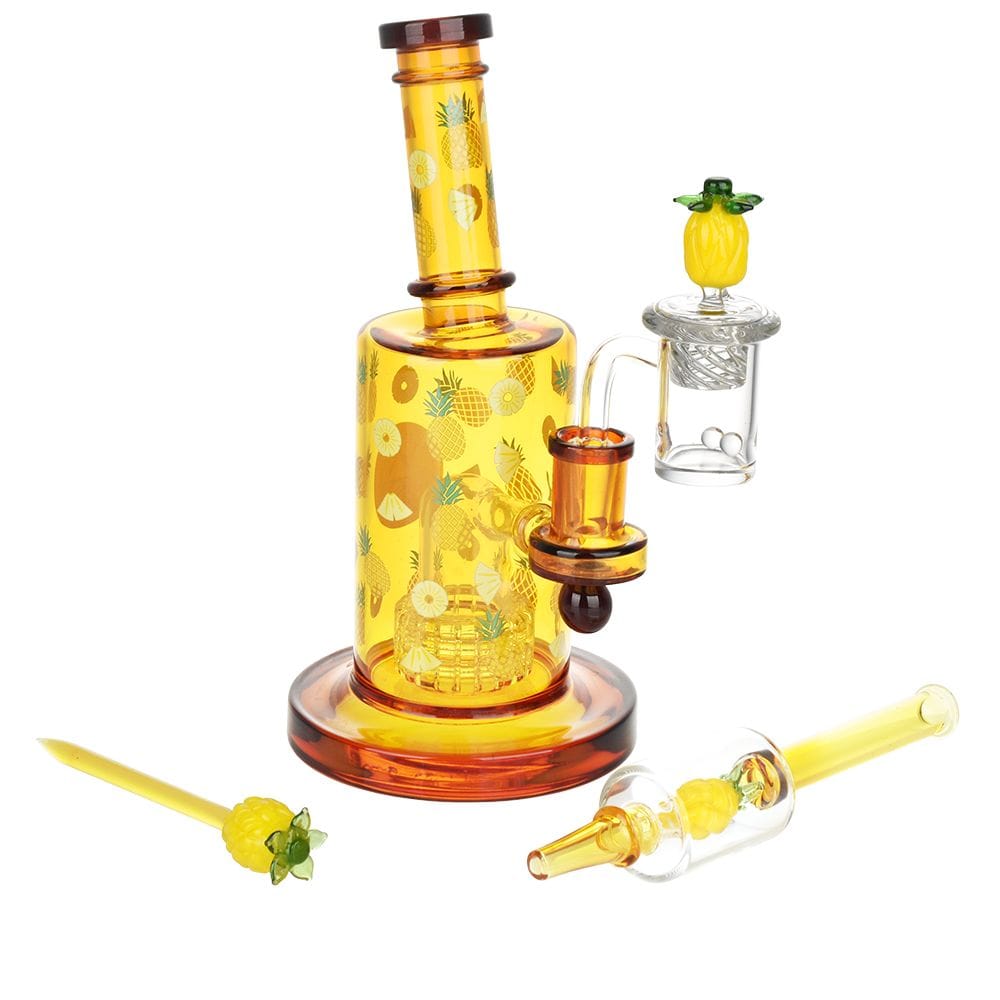 Front three-quarter view of the Pulsar Fruit Series Pineapple Express Glow In The Dark Dab Rig Kit - 8" / 14Mm F, showing a yellow pineapple-patterned 8" glass rig with matching pineapple-themed accessories on a white background