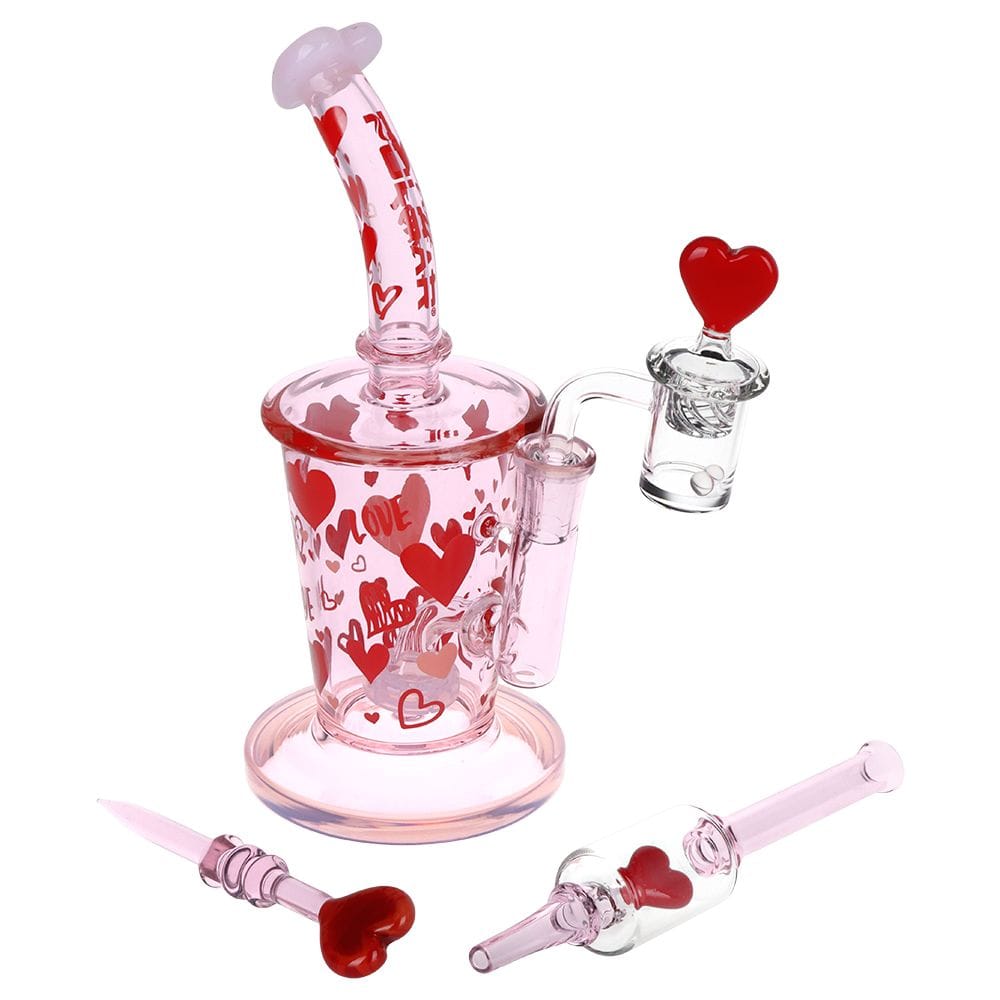 Angled front view of the Pulsar Valentine'S Love Hearts Glass Dab Rig Set - 8.5" / 14Mm F, showing a pink glass rig covered in red hearts with matching heart-topped accessories on a white background