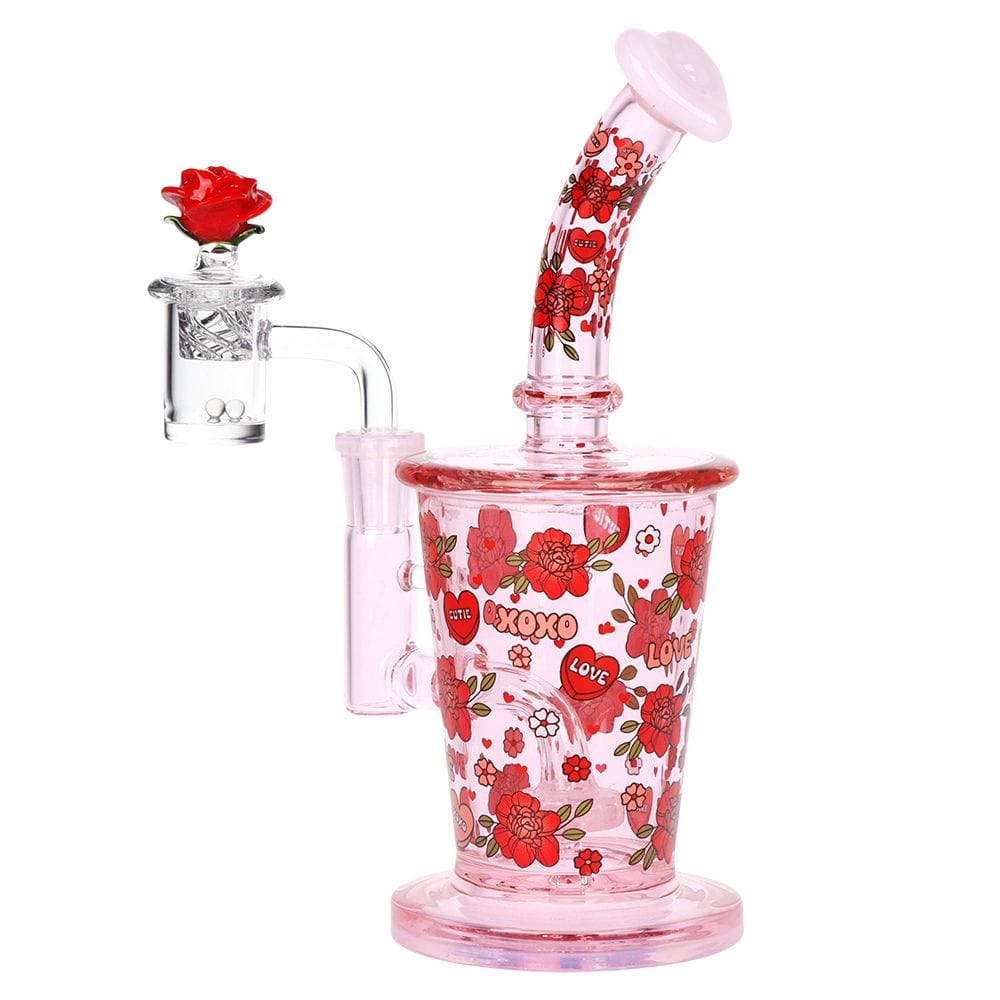 Front three-quarter view of the Pulsar Valentine'S Rose Glass Dab Rig Set - 8.25" / 14Mm F, a pink glass rig decorated with red roses and heart motifs.