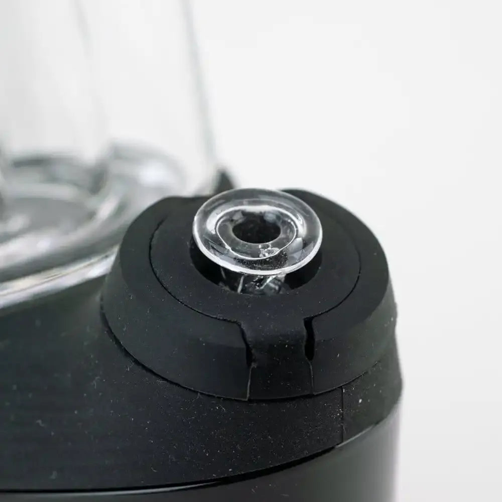 Close-up of the clear Empire Glassworks PuffCo 'New Peak' & Proxy Glass Joystick Cap seated in a black rubberized base against a soft white background