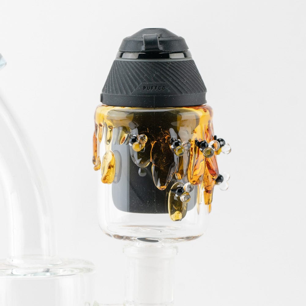 A close-up, angled view of the Bee PuffCo Proxy 14m Glass Attachment, showcasing its transparent glass and unique bulbous design.