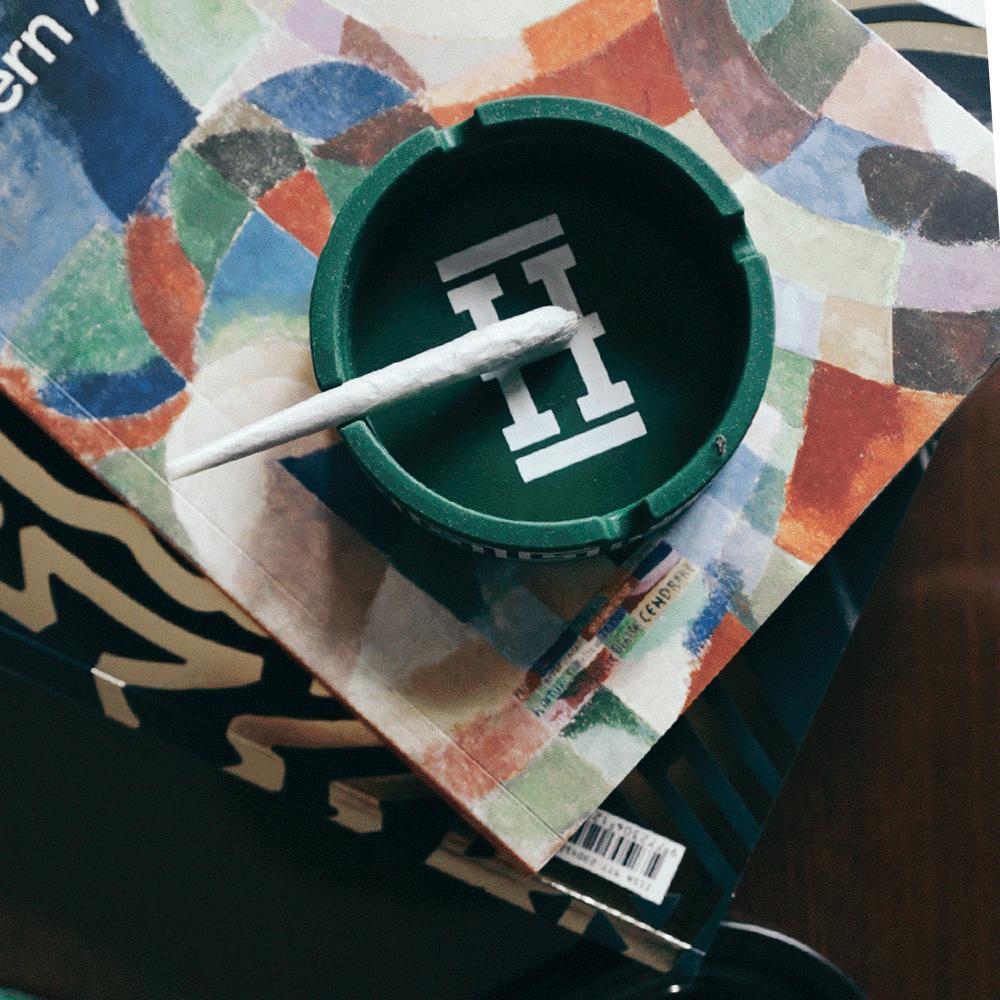 Overhead view of the Asher "Cannaflage" Silicone Ashtray, showcasing a dark, circular design against a colorful, patterned backdrop.