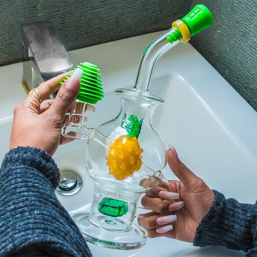 A close-up shot of a hand inserting the green HEMPER Tech Cleaning Plugs+Caps into the joint of a clear glass piece.