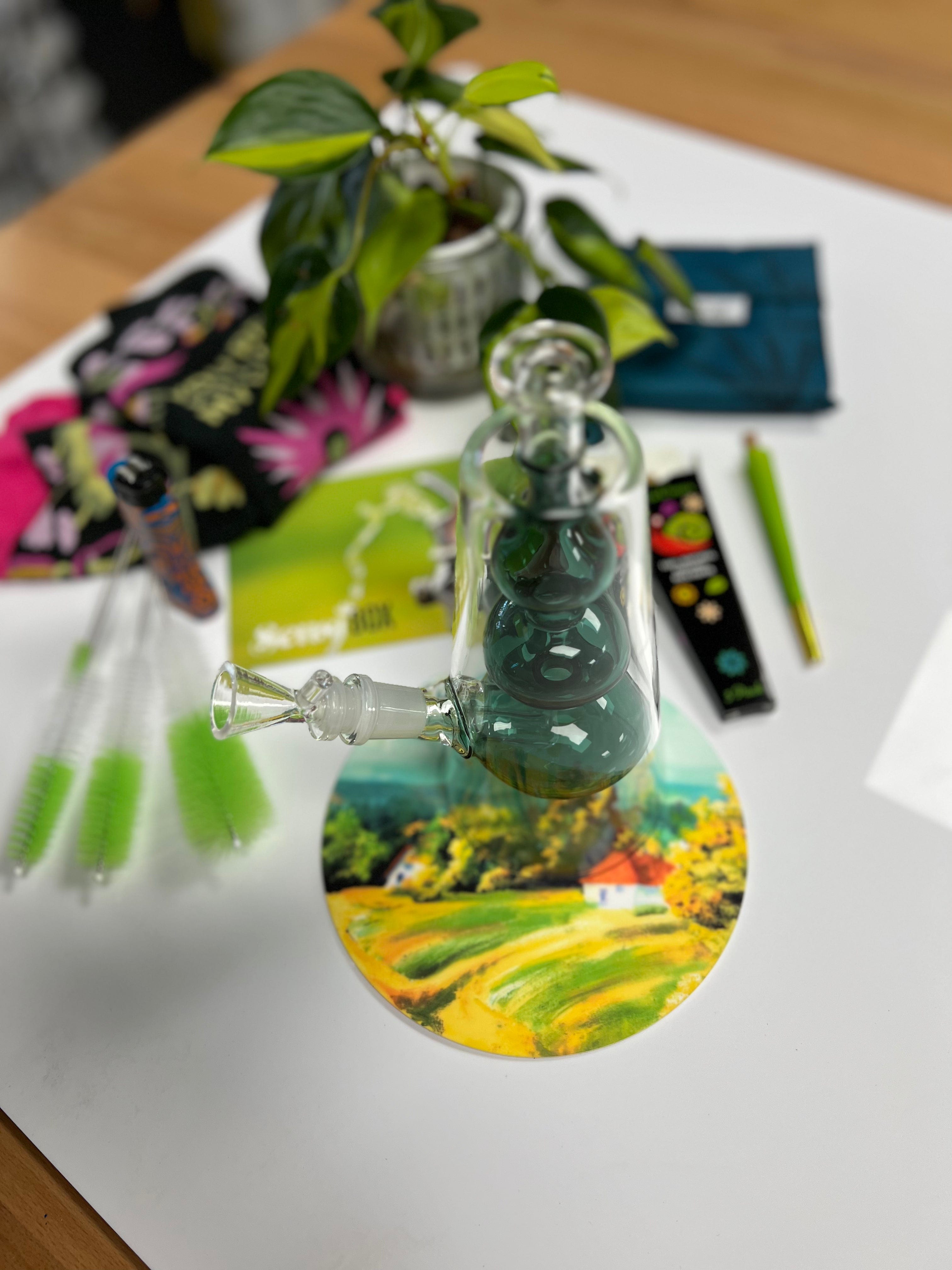 A close-up view of The Bubblah, showcasing its unique shape alongside vibrant packaging and blurred greenery.